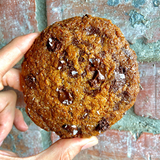 Hand holding a large OldJoy Double  chocolate chip cookie with a rustic background